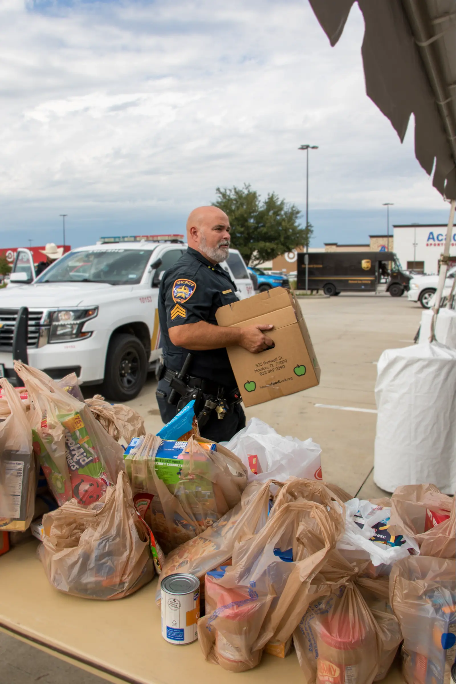 A sheriff’s deputy carries a box of food past tables of groceries.