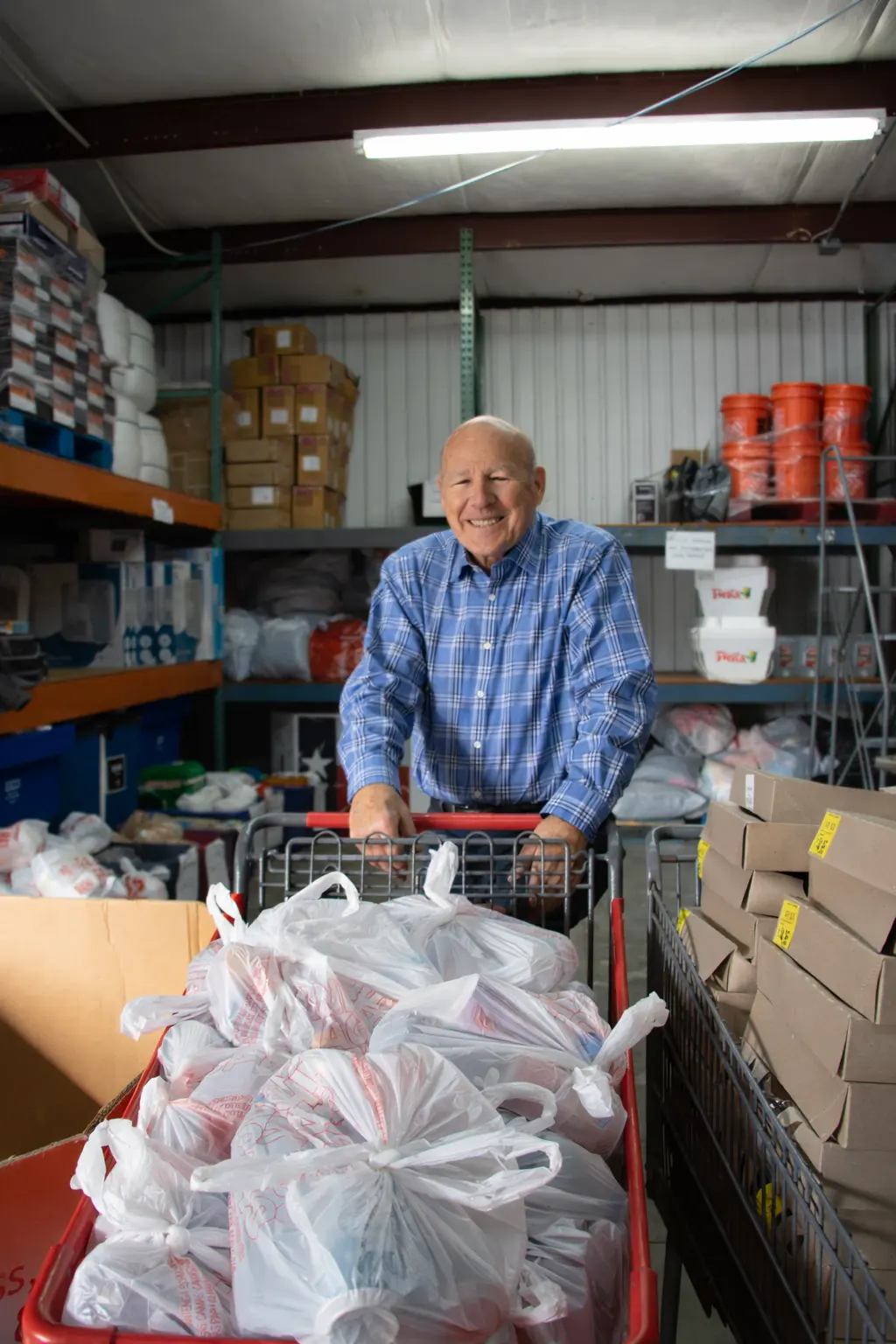 A volunteer pushes a cart of grocery bags through the warehouse.