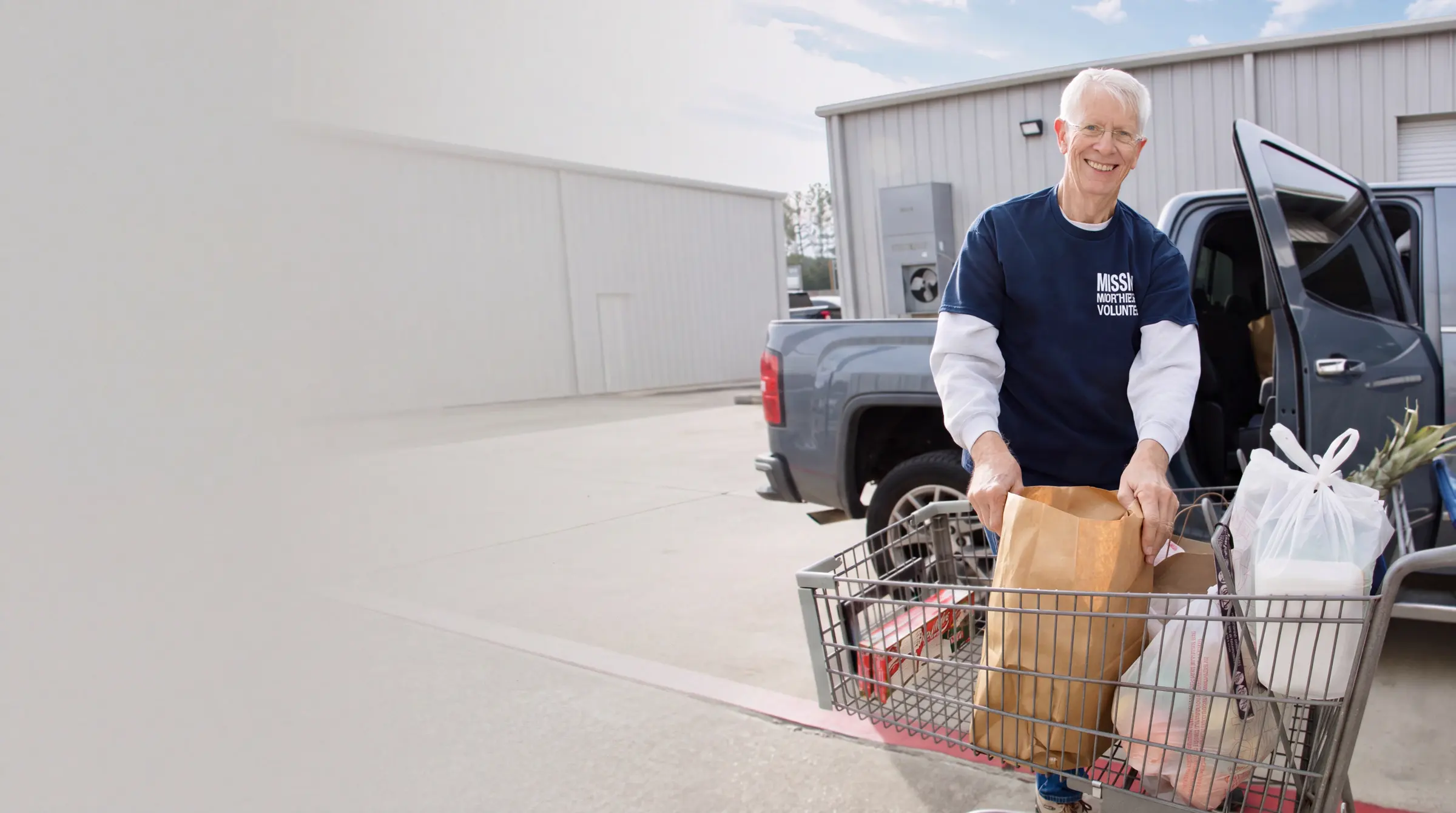 A volunteer loads grocery bags from a cart into a pickup outside the warehouse.