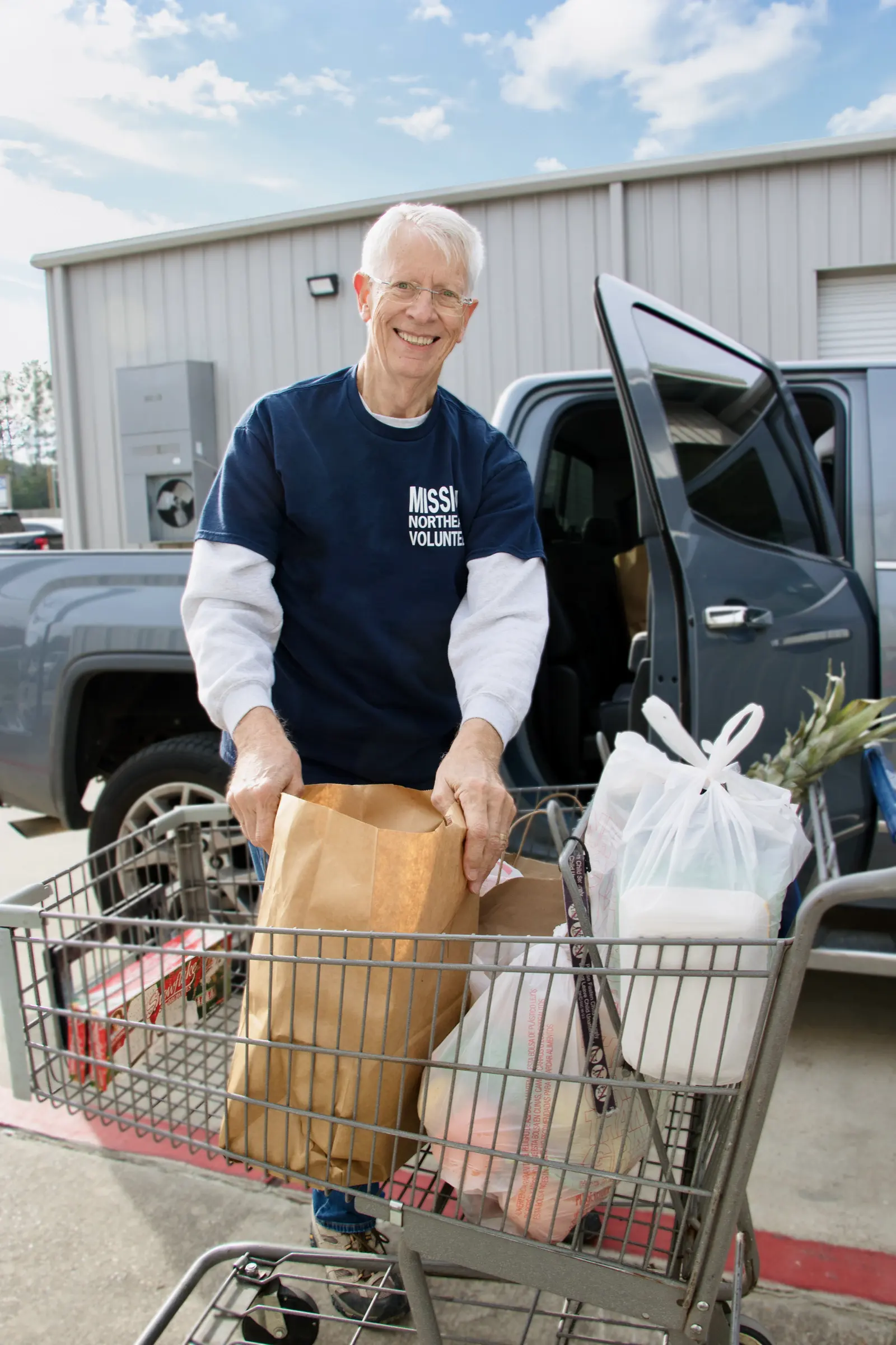 A volunteer in a Mission Northeast shirt loads grocery bags from a cart.