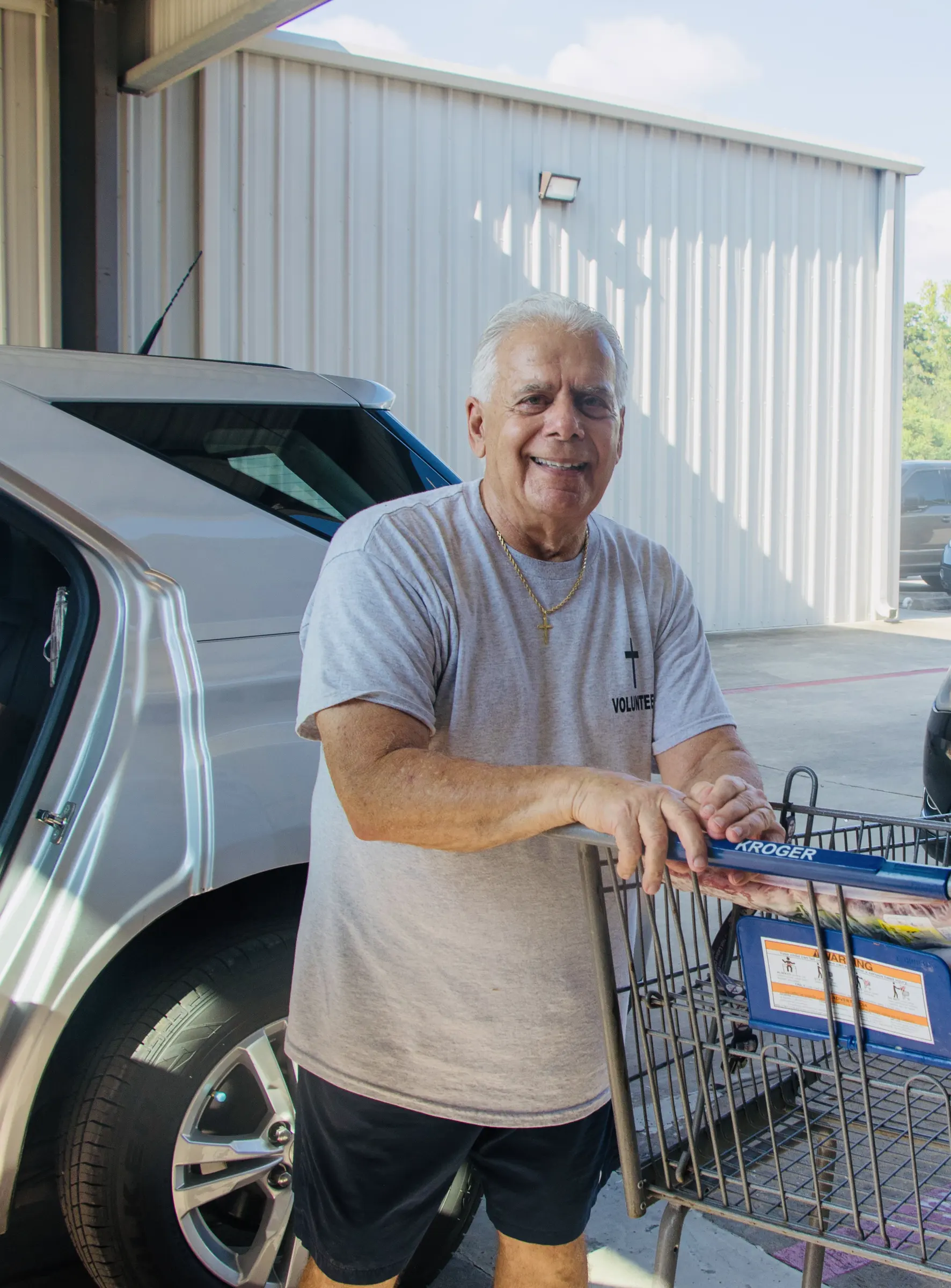 A volunteer stands with a Kroger cart beside a car at the mission.