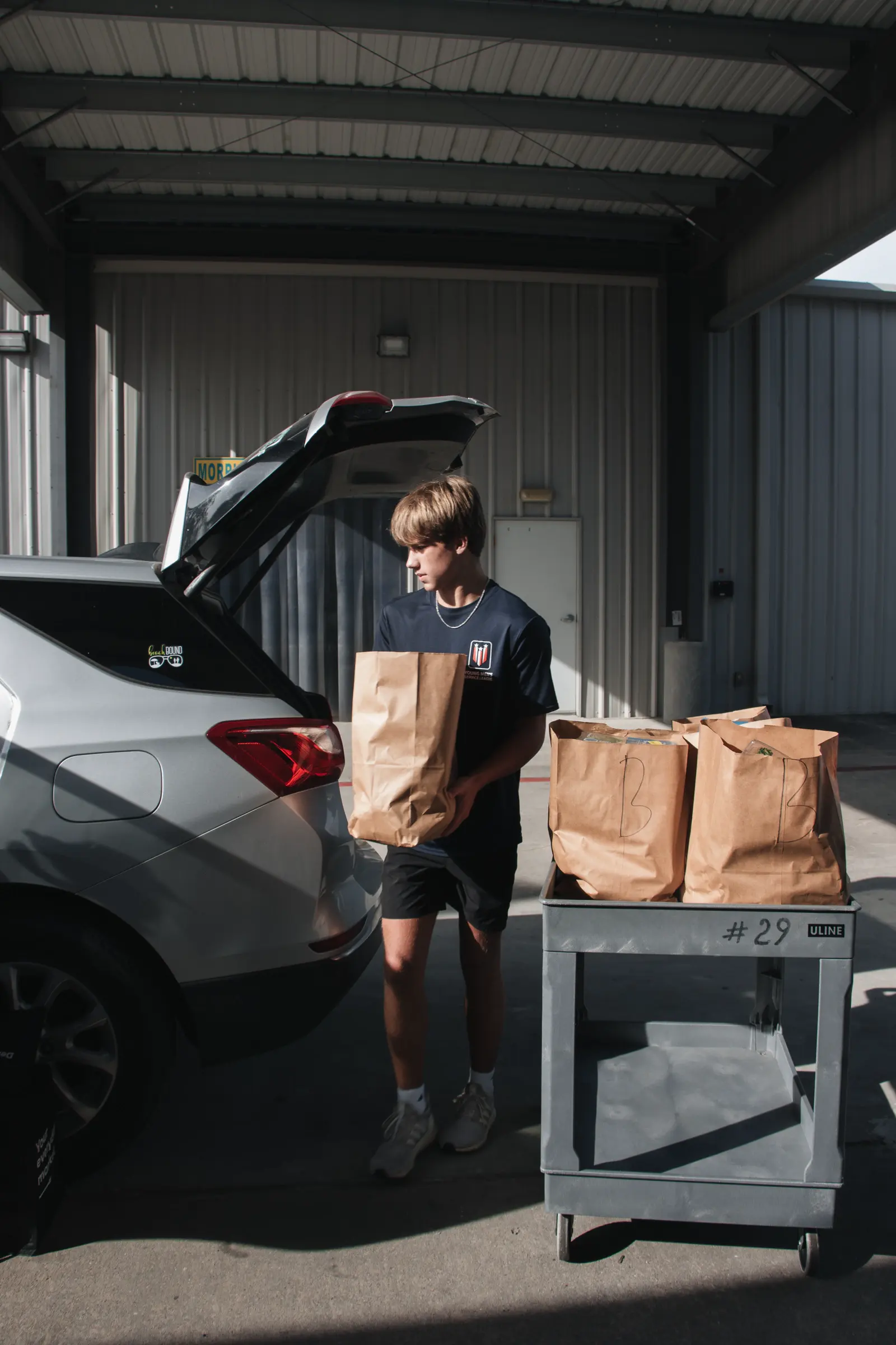 A volunteer carries paper grocery bags to an open car.